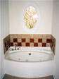 Decorative oval window above a whirlpool tubs adds to the focal point of this master bathroom 